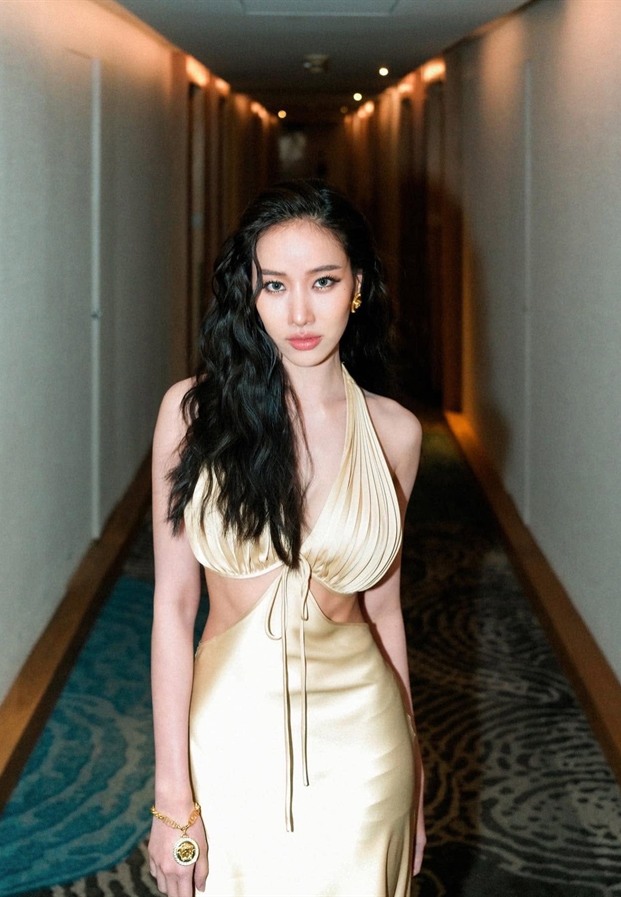Mook Pichana ยืนกลางทางเดินโรงแรมในชุดราตรีสีทอง