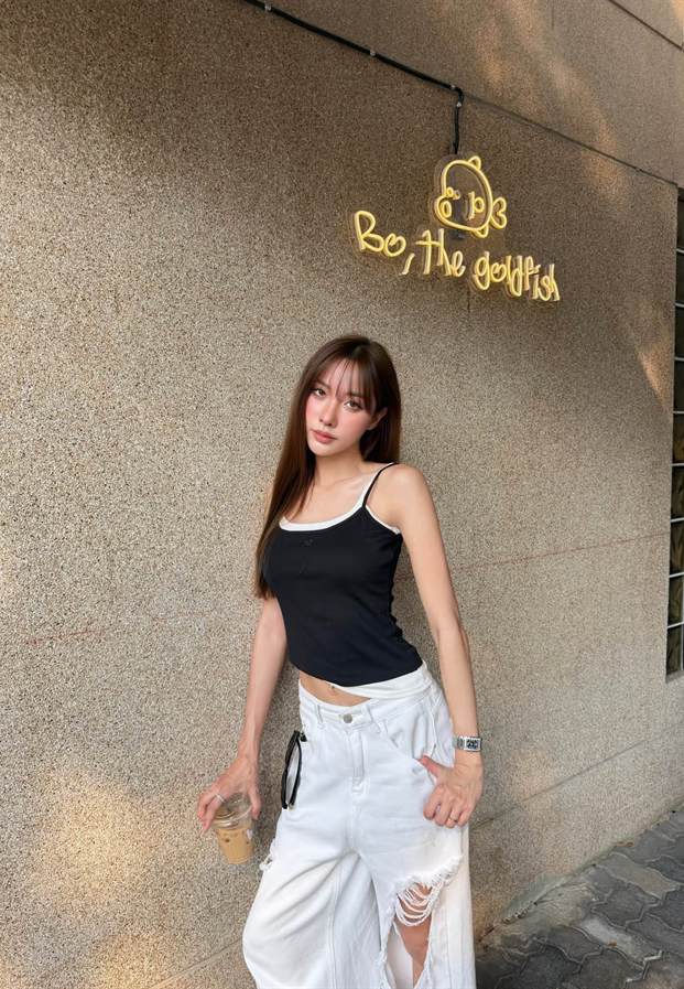 ยืนหน้าผนังปูนกับป้ายไฟในเสื้อกล้ามสีดำ