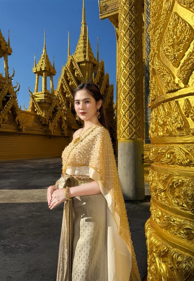 ยืนหน้าโบสถ์สีทองในชุดไทยโทนครีม