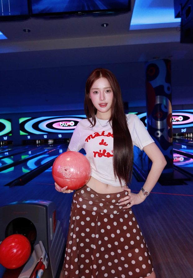 ขนม Khanomwws ถือลูกโบว์ลิ่งสีแดงในลานโบว์ลิ่งไฟนีออน