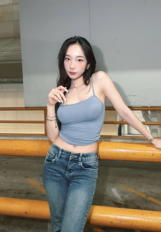 ยืนในเสื้อสายเดี่ยวสีฟ้าอมเทากับกางเกงยีนส์