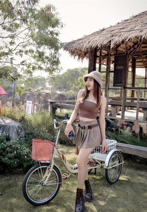 ลุคเกาะอกสีน้ำตาลคู่กระโปรงสั้นลายสก็อตคาดเข็มขัดและหมวกบักเก็ตถักบนจักรยานสามล้อในสวน