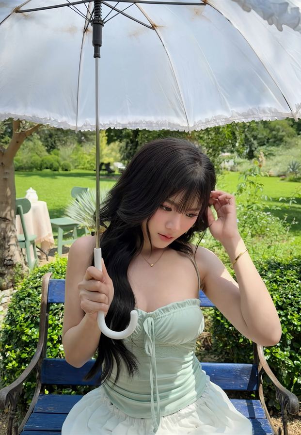Prim Benjawan กางร่มลูกไม้สีขาวนั่งบนม้านั่งในสวน
